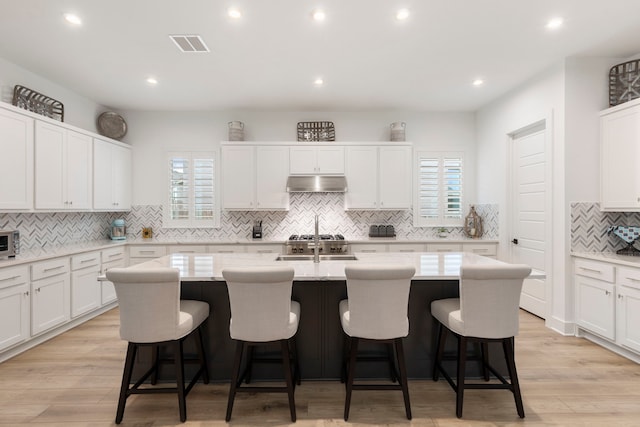 kitchen featuring a breakfast bar, white cabinets, light hardwood / wood-style flooring, and a kitchen island with sink