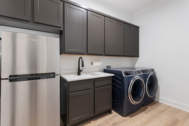 laundry room with cabinets, sink, washer and dryer, and light hardwood / wood-style floors