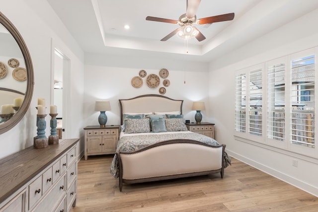 bedroom with ceiling fan, a tray ceiling, and light hardwood / wood-style flooring