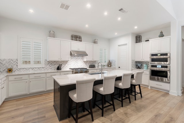 kitchen with white cabinets, double oven, and a center island with sink