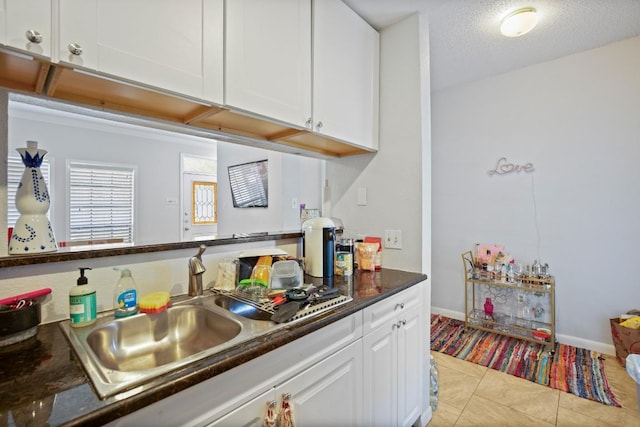 715 22 1/2 St Unit 101, Austin, TX 78705 - kitchen with white cabinets, a sink, dark countertops, light tile patterned flooring, and baseboards