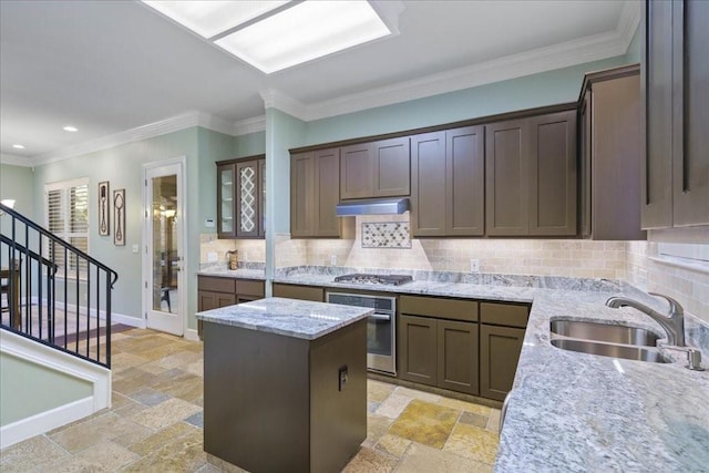 kitchen with appliances with stainless steel finishes, a center island, light stone countertops, ornamental molding, and sink