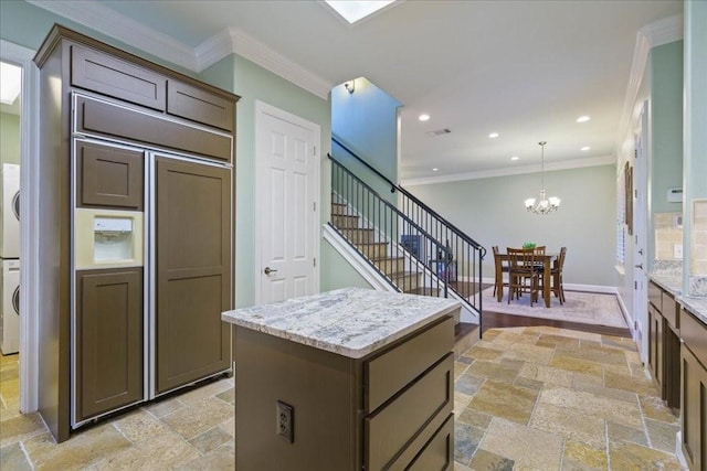 kitchen featuring light stone counters, a notable chandelier, ornamental molding, and a center island