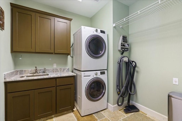laundry room with a sink, baseboards, stone finish floor, cabinet space, and stacked washer / drying machine