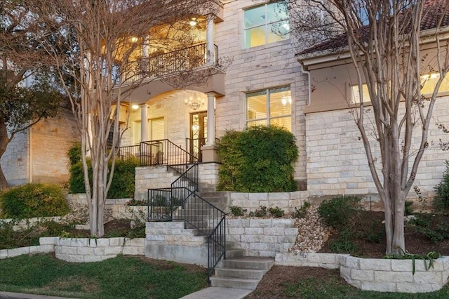 exterior space featuring covered porch, stone siding, stairs, and a balcony