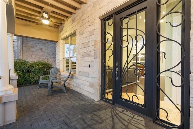property entrance featuring stone siding, a ceiling fan, and covered porch