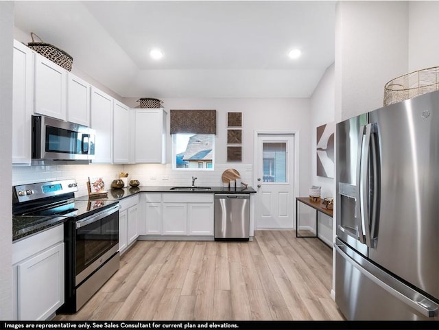 kitchen featuring light wood-style flooring, a sink, appliances with stainless steel finishes, dark countertops, and backsplash