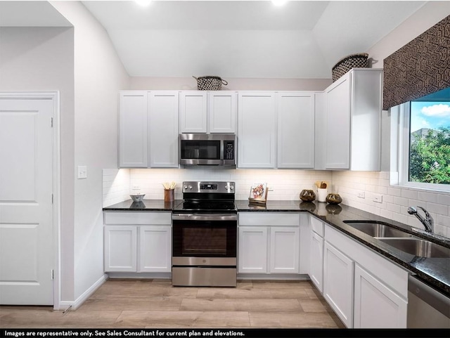 kitchen featuring decorative backsplash, stainless steel appliances, vaulted ceiling, light wood finished floors, and a sink
