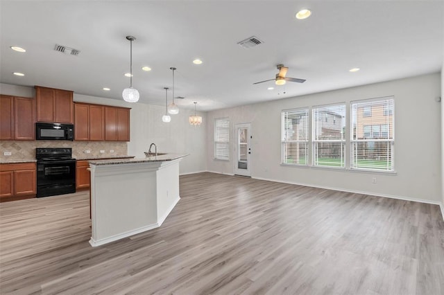 kitchen with black appliances, decorative light fixtures, a center island with sink, and light wood-type flooring