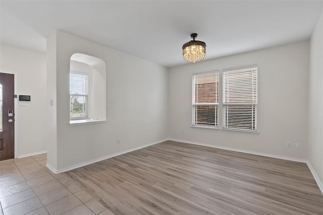 unfurnished room featuring light wood finished floors, arched walkways, baseboards, and a chandelier