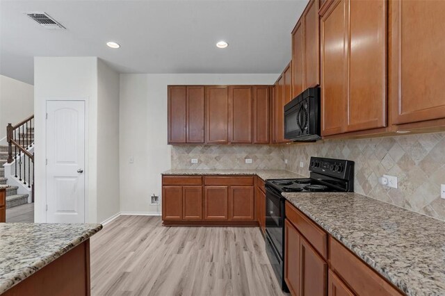 kitchen with light stone countertops, decorative backsplash, light wood-type flooring, and black appliances