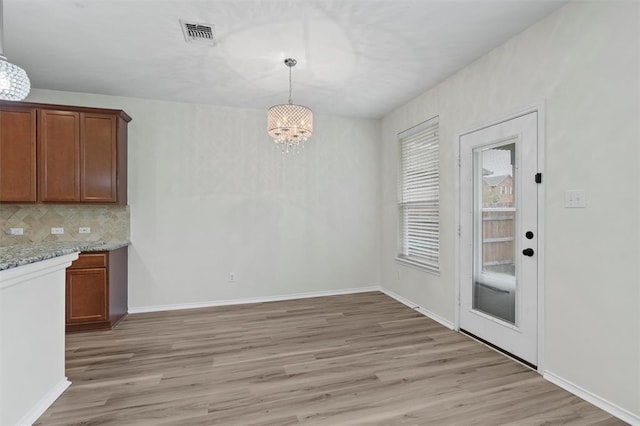 unfurnished dining area with light wood-type flooring, an inviting chandelier, baseboards, and visible vents