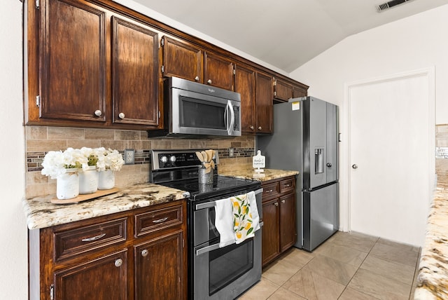 kitchen featuring light stone countertops, appliances with stainless steel finishes, tasteful backsplash, vaulted ceiling, and light tile patterned flooring