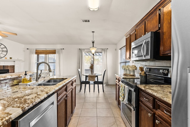 kitchen with a brick fireplace, stainless steel appliances, sink, light tile patterned floors, and decorative light fixtures