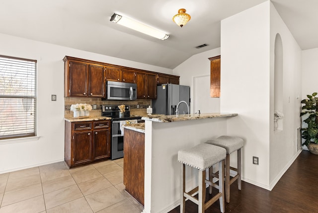 kitchen with kitchen peninsula, a kitchen bar, stainless steel appliances, light tile patterned floors, and lofted ceiling