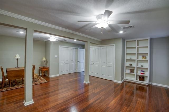 basement featuring a textured ceiling, dark wood-type flooring, ornamental molding, and built in shelves