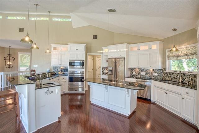 kitchen with appliances with stainless steel finishes, a kitchen island, sink, white cabinetry, and tasteful backsplash