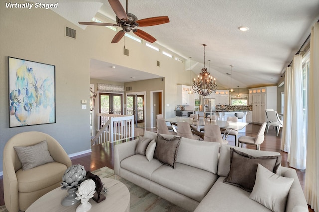 living room with ceiling fan with notable chandelier, high vaulted ceiling, a textured ceiling, and hardwood / wood-style floors