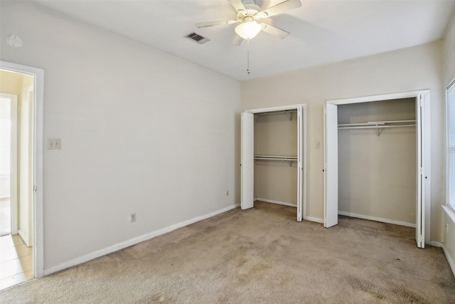 unfurnished bedroom featuring multiple closets, ceiling fan, and light carpet