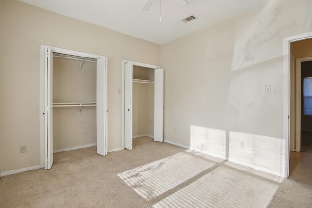 unfurnished bedroom featuring ceiling fan, light colored carpet, and two closets