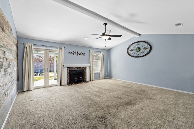 unfurnished living room with french doors, lofted ceiling with beams, a stone fireplace, carpet flooring, and ceiling fan