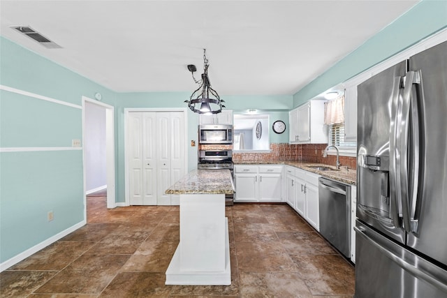 kitchen with appliances with stainless steel finishes, sink, pendant lighting, white cabinets, and a kitchen island