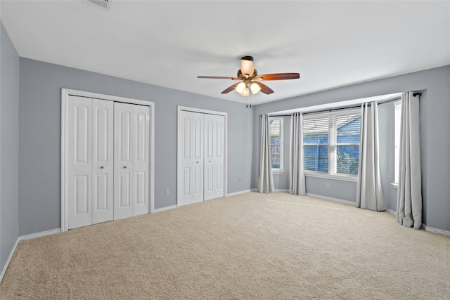 unfurnished bedroom with ceiling fan, light carpet, and two closets