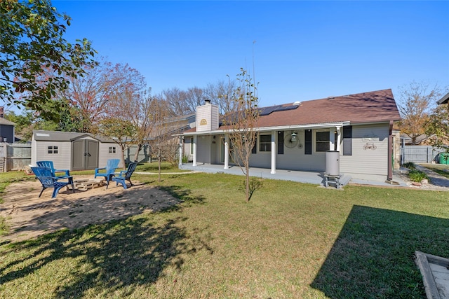 back of house with a lawn, a fire pit, solar panels, a storage shed, and a patio