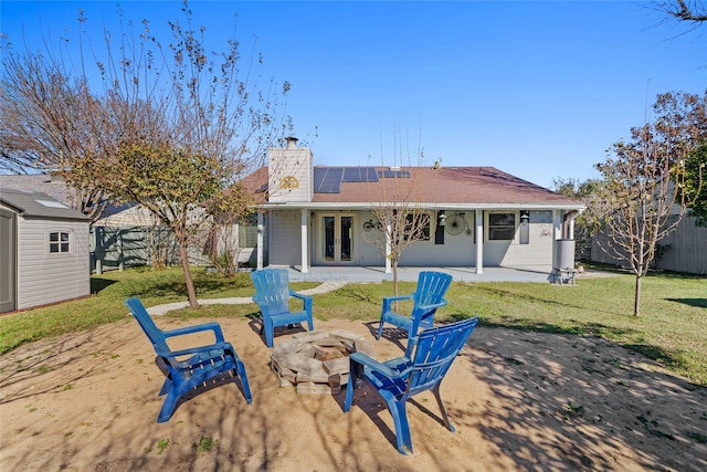 rear view of house featuring solar panels, a storage shed, a yard, a patio, and an outdoor fire pit