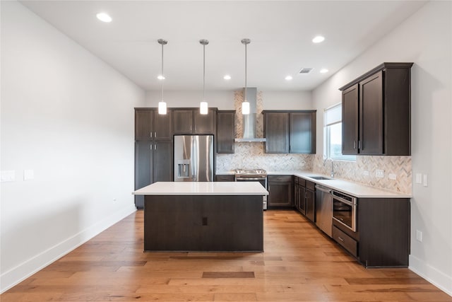 kitchen featuring sink, wall chimney exhaust hood, stainless steel appliances, decorative light fixtures, and a kitchen island