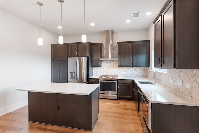 kitchen with sink, a center island, wall chimney range hood, decorative light fixtures, and appliances with stainless steel finishes