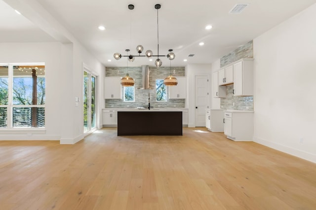 kitchen with backsplash, a kitchen island with sink, hanging light fixtures, and white cabinets