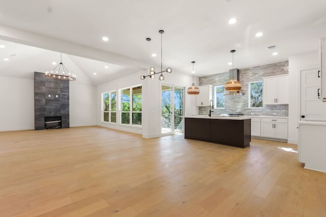 kitchen with white cabinetry, hanging light fixtures, a kitchen island, decorative backsplash, and light wood-type flooring