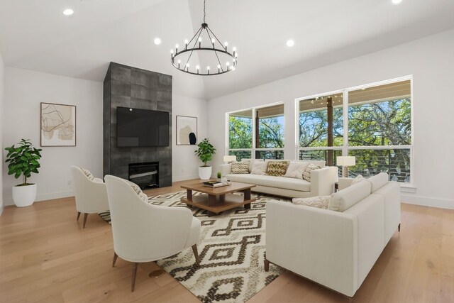 living room featuring a tile fireplace, vaulted ceiling, a chandelier, and light hardwood / wood-style floors