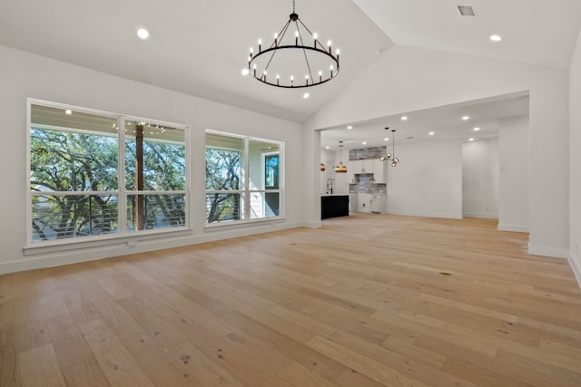 unfurnished living room featuring a notable chandelier, light hardwood / wood-style flooring, and high vaulted ceiling