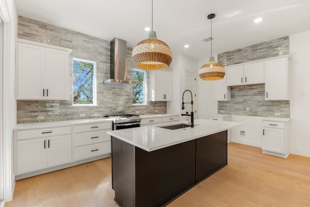 kitchen with wall chimney range hood, decorative light fixtures, an island with sink, and white cabinets