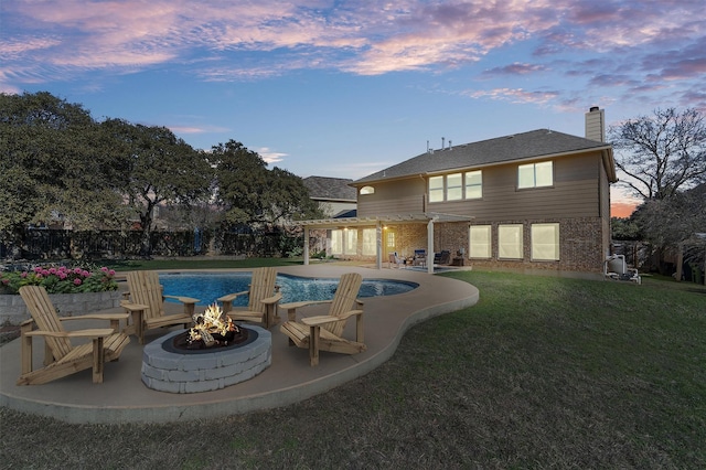 pool at dusk featuring a lawn, a patio area, and an outdoor fire pit