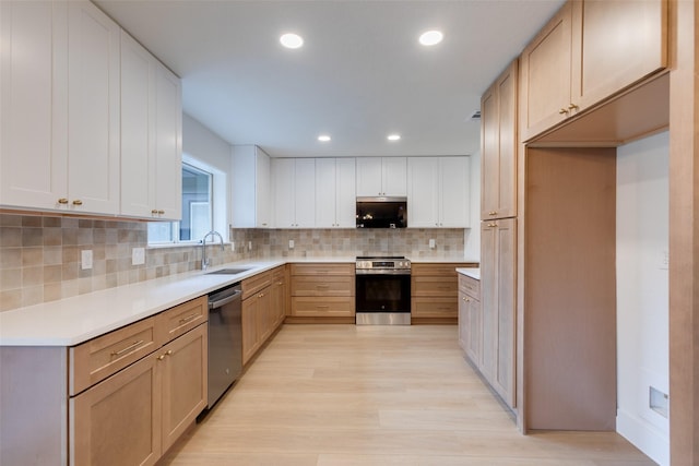 kitchen featuring appliances with stainless steel finishes, backsplash, light hardwood / wood-style flooring, and sink