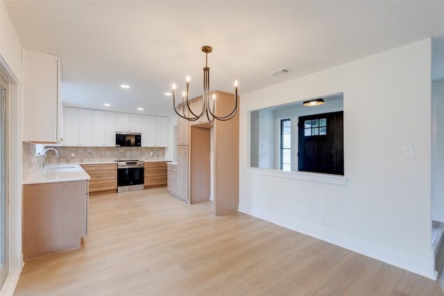 kitchen featuring backsplash, sink, decorative light fixtures, stainless steel range oven, and white cabinetry