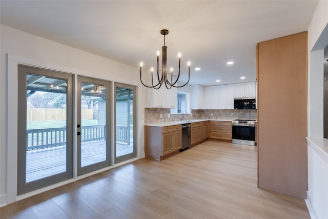 kitchen with appliances with stainless steel finishes, backsplash, pendant lighting, an inviting chandelier, and white cabinetry