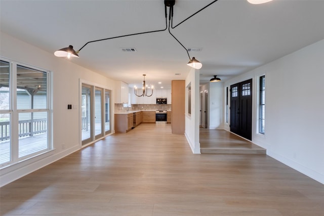 kitchen with tasteful backsplash, stainless steel appliances, decorative light fixtures, a notable chandelier, and light hardwood / wood-style floors