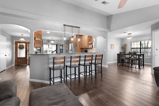 kitchen with ceiling fan, dark hardwood / wood-style floors, light stone countertops, kitchen peninsula, and stainless steel refrigerator