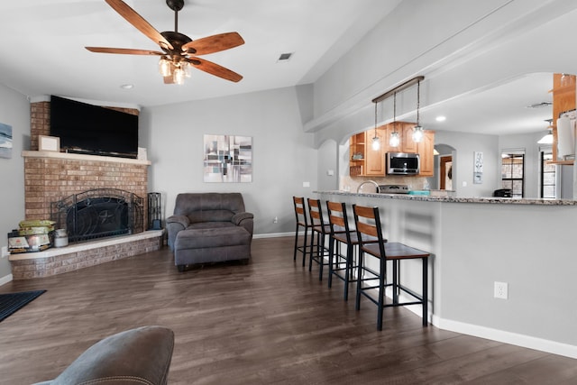 kitchen with light stone countertops, a brick fireplace, ceiling fan, pendant lighting, and a breakfast bar area