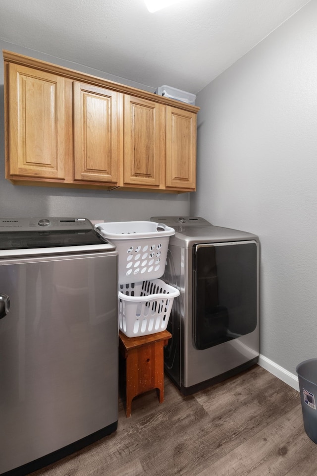 clothes washing area featuring washing machine and clothes dryer, dark hardwood / wood-style flooring, and cabinets