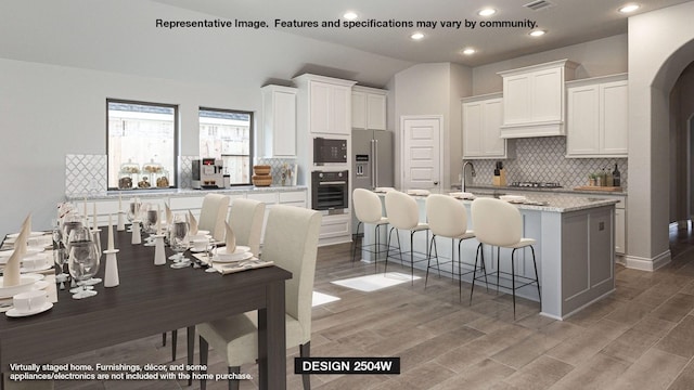 kitchen with black appliances, a center island with sink, a breakfast bar area, white cabinetry, and lofted ceiling