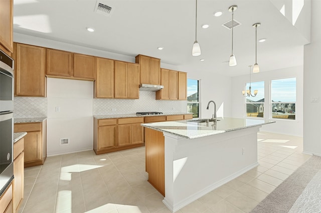 kitchen with an inviting chandelier, light tile patterned floors, light stone countertops, a center island with sink, and pendant lighting