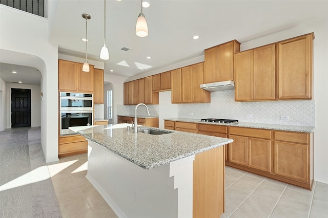 kitchen with sink, a center island with sink, stainless steel appliances, and light stone countertops