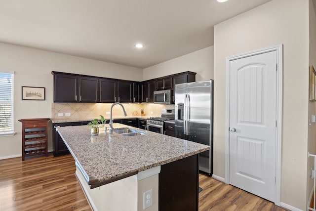 kitchen with sink, appliances with stainless steel finishes, dark hardwood / wood-style floors, light stone countertops, and a kitchen island with sink