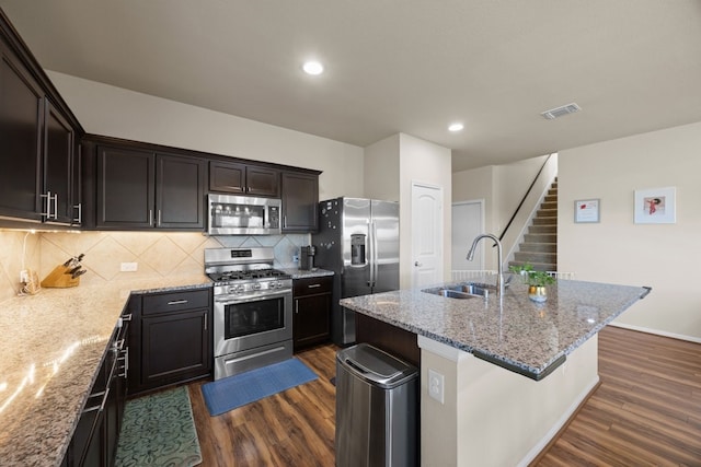 kitchen featuring sink, a center island with sink, appliances with stainless steel finishes, dark hardwood / wood-style floors, and light stone countertops