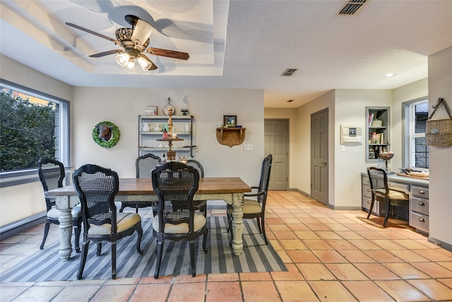 tiled dining space featuring a tray ceiling, ceiling fan, and a textured ceiling